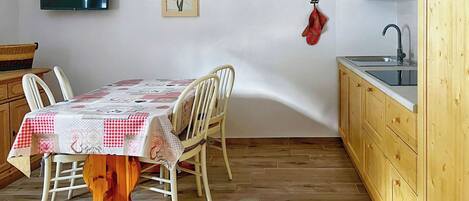 Un comedor con una mesa dispuesta para cuatro personas, sillas de madera, una mesa de madera, una cocina con armarios de madera, un microondas y un lavabo.