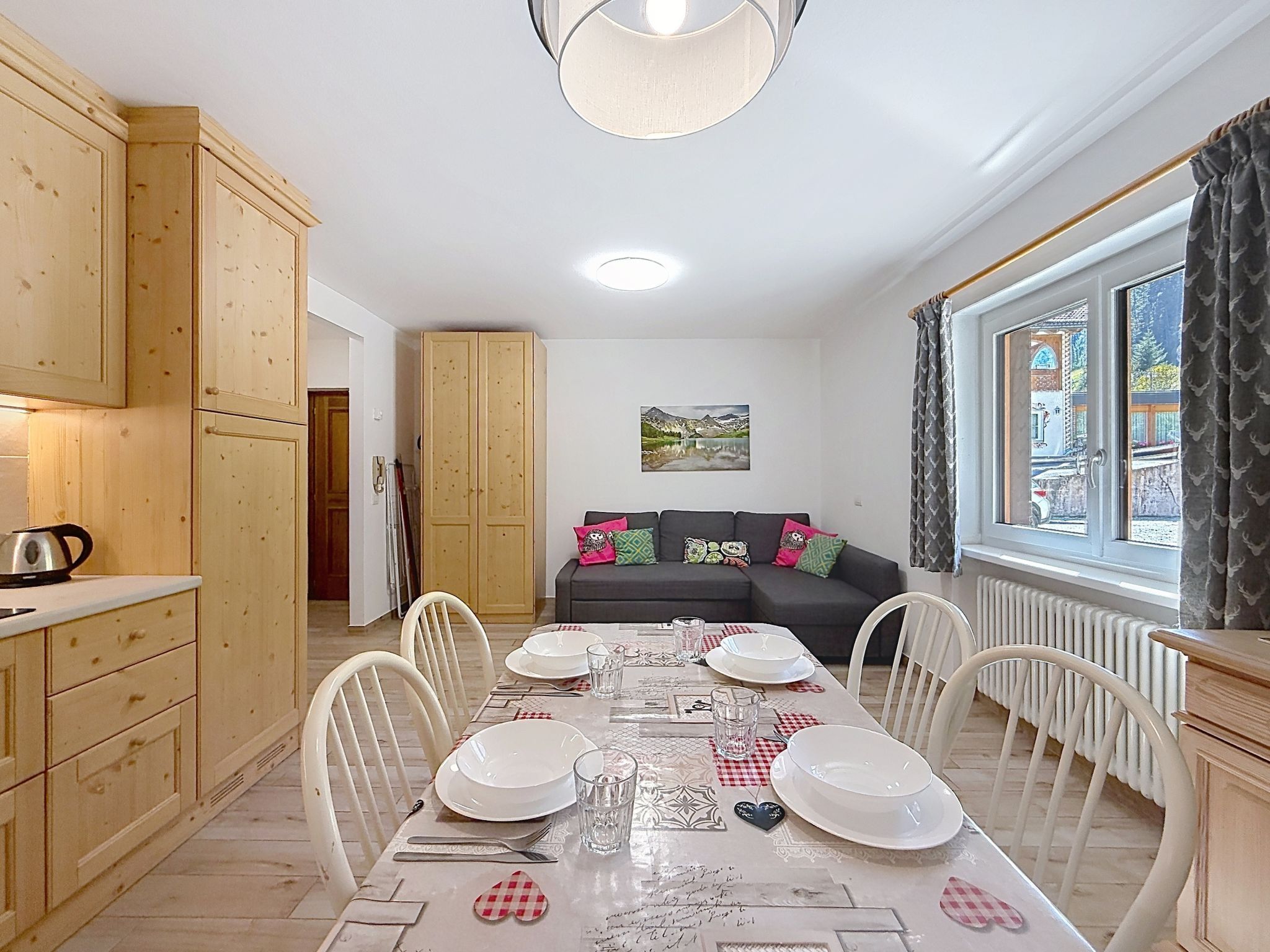 Un coin repas avec une table dressée pour quatre personnes, des meubles en bois, un canapé avec des coussins et une fenêtre avec des rideaux.