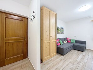 Ein Zimmer mit Holztür, einem Schrank, einem grauen Sofa mit bunten Kissen und einem Bild an der Wand.