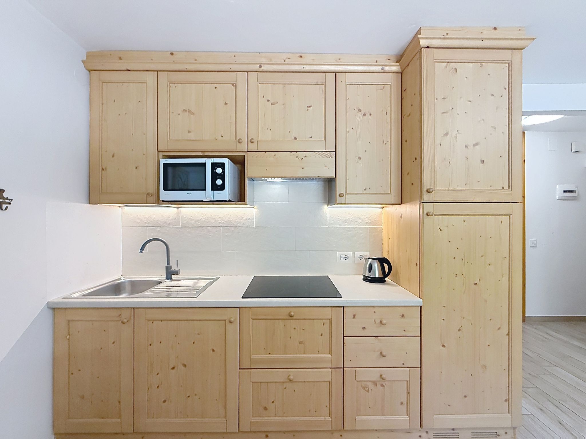 Una cucina compatta con mobili in legno, un forno a microonde integrato, un lavandino e un bollitore.