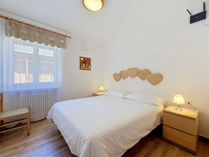 Ein Schlafzimmer mit einem Bett, Nachttischen, einem Sessel, einem Fenster mit Vorhängen und einer Wandleuchte.
