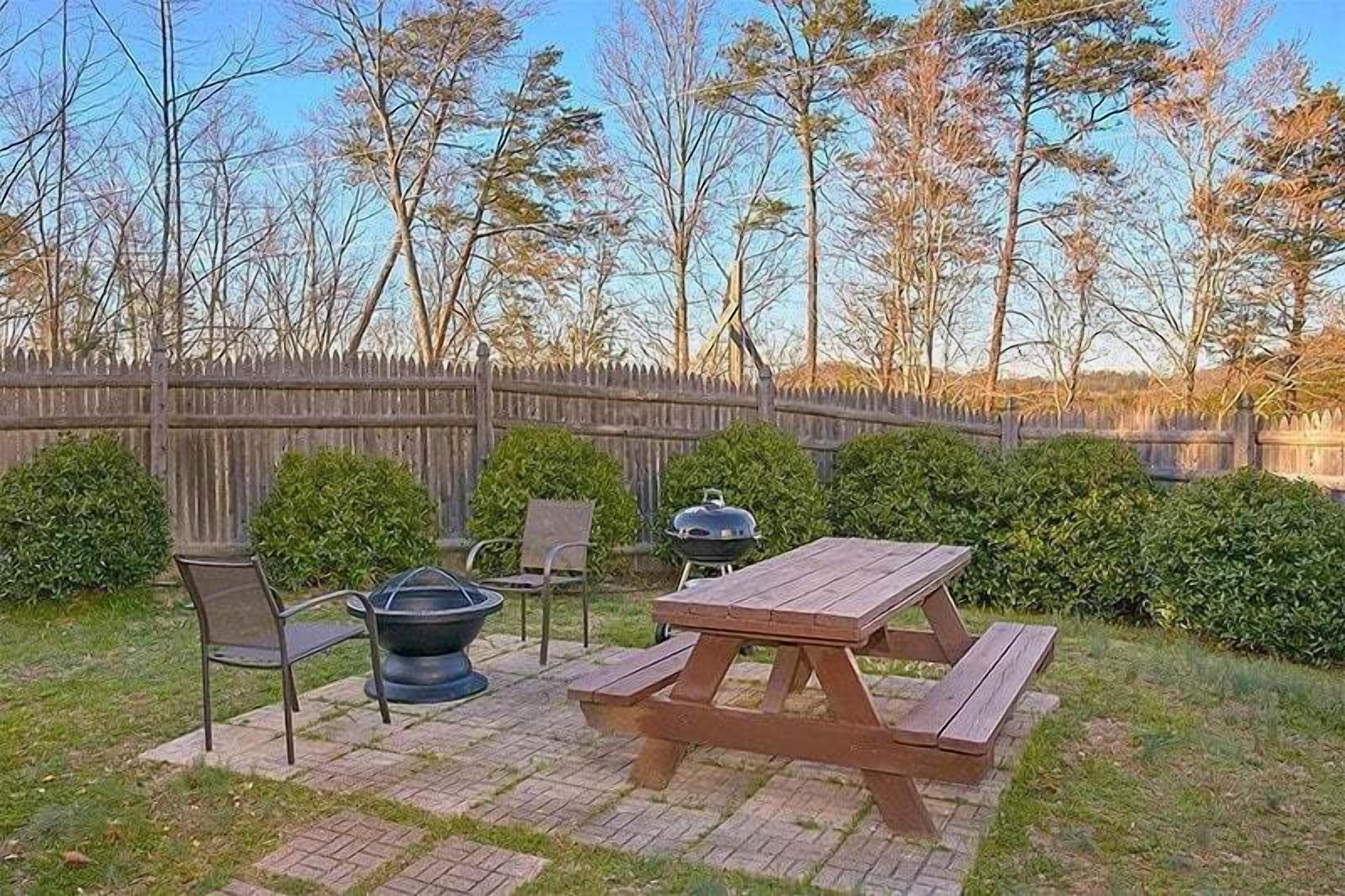 Un patio al aire libre con una mesa de picnic, sillas y una parrilla.
