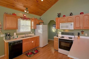 A compact kitchen with wooden cabinets, a microwave, a refrigerator, and a dishwasher. - A Dream Come True | Mountain Views | Hot Tub | Fire Pit (Pigeon Forge)