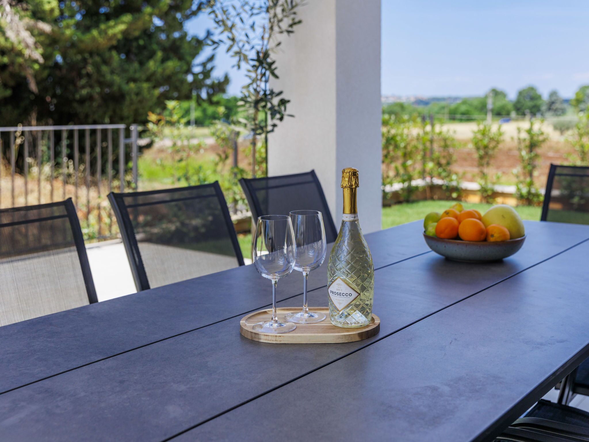 A table with a bottle of Prosecco, two glasses, and a bowl of fruit.