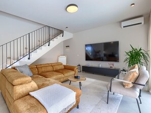 A modern living room with a staircase, a sectional sofa, a coffee table, a TV, and a plant. - Vacation home Riata by Interhome (Poreč)
