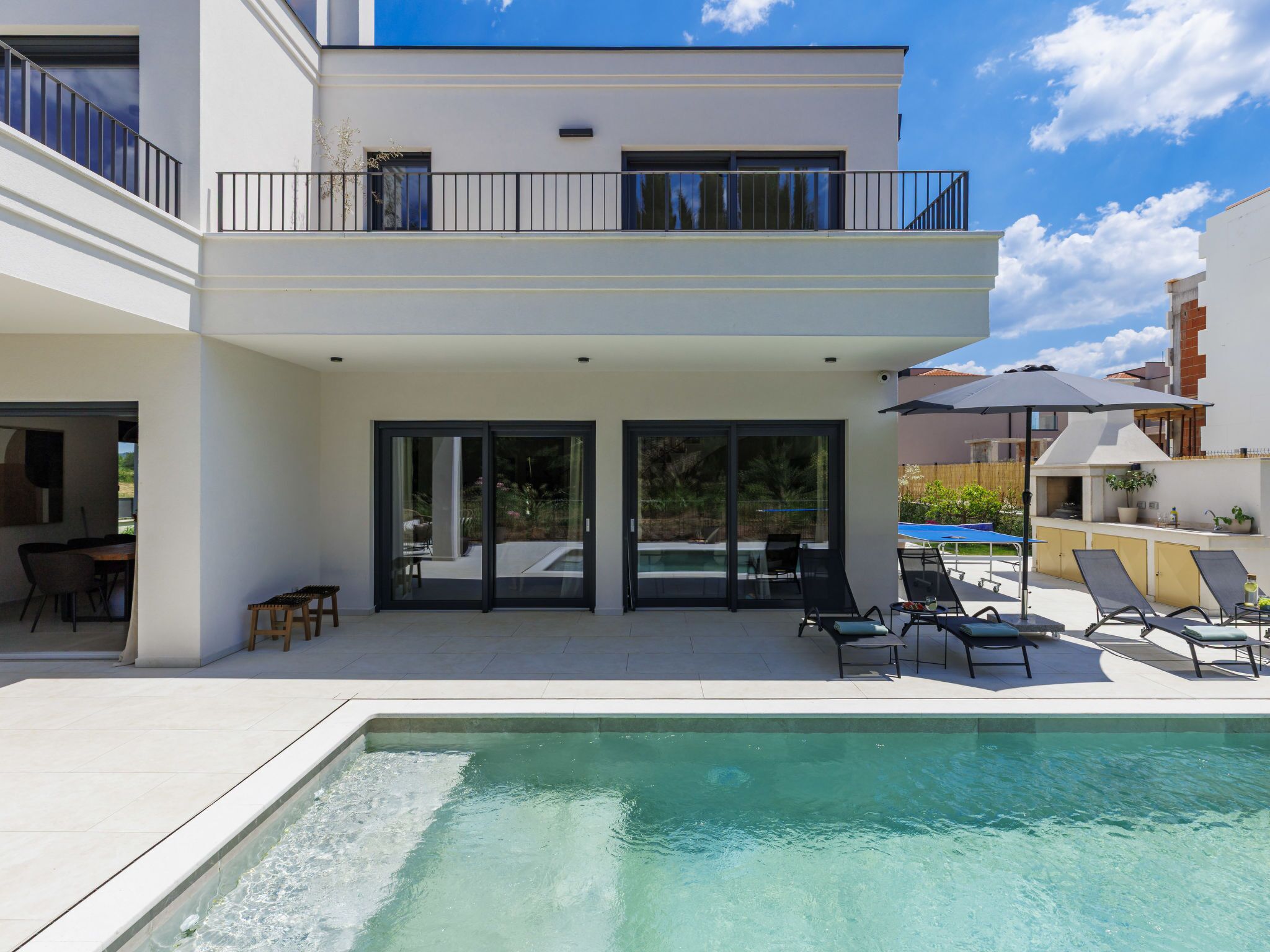 A modern two-story building with a swimming pool, outdoor seating, and a covered patio area.
