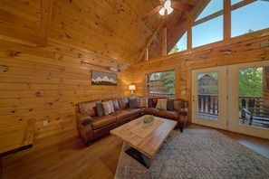 A wooden cabin interior with a leather couch, a wooden coffee table, and a large window. - A Mountain Lodge | Hot Tub | Game Room (Pigeon Forge)