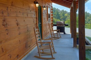 A wooden cabin with a porch, a grill, and rocking chairs. - A Mountain Palace | Theater Room | Hot Tub (Pigeon Forge)