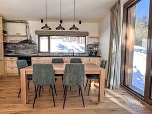 A modern kitchen with a large dining table, wooden cabinets, and a view of a snowy landscape. - Rebelka by Interhome (Horni Misecky)