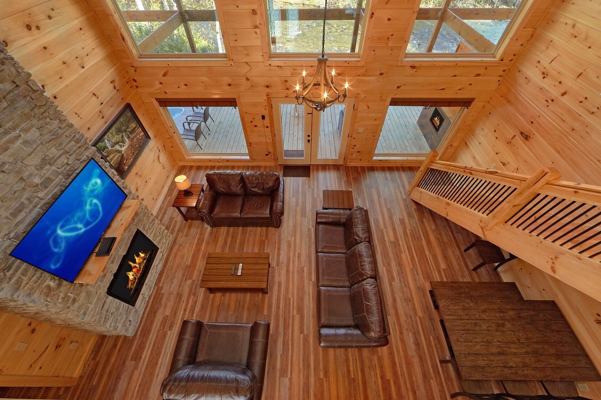 A spacious wooden cabin interior with a high ceiling, a fireplace, leather sofas, and a television.