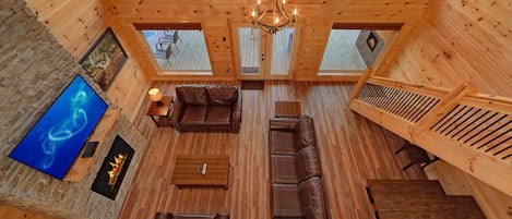 A spacious wooden cabin interior with a high ceiling, a fireplace, leather sofas, and a television.
