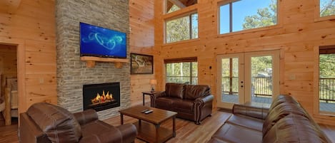 Amplia sala de estar con chimenea de piedra, sofás de cuero, una mesa de centro y un televisor de pantalla plana montado en la pared.