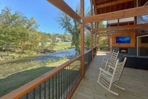 A wooden deck with a view of a river, a fireplace, and a television. - A River Retreat | Private Pool | Hot Tub | River Views (Pigeon Forge)
