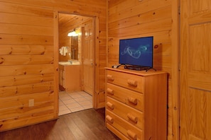 A wooden interior with a television on a dresser, a bathroom with a mirror and towel rack, and a tiled floor. - A Rocky Top Ridge | Hot Tub | Game Room (Wears Valley)
