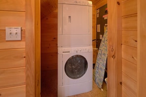 A compact laundry area with a stacked washer and dryer, a power outlet, and a wooden wall. - A Rocky Top Ridge | Hot Tub | Game Room (Wears Valley)