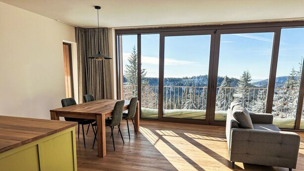 A spacious room with a large dining table, a sofa, and a view of a snowy landscape through large windows. - Rebelka by Interhome (Horni Misecky)