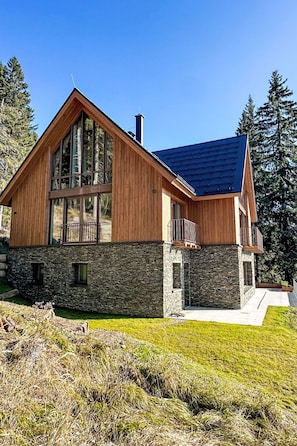 Ein modernes, zweistöckiges Haus mit Stein Fundament und Holzfassade, mit großen Fenstern und einem Balkon.