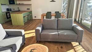A modern living room with a grey sofa, a round wooden coffee table, and a dining area with a wooden table and chairs. - Rebelka by Interhome (Horni Misecky)