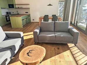 Ein modernes Wohnzimmer mit einer grauen Couch, einem runden Couchtisch und einem Essbereich mit Holztisch und Stühlen.