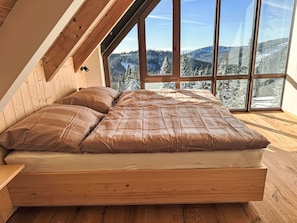 Ein Schlafzimmer mit einem hölzernen Bett, großen Fenstern und Blick auf schneebedeckte Berge.