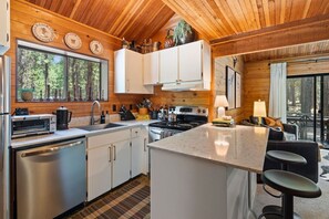 A modern kitchen with white cabinets, stainless steel appliances, and a central island with bar stools. - Trail One | Black Butte Ranch | Sleeps 8 | Family (Sisters)