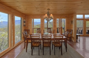 A wooden dining room with a chandelier, large windows, and a view of mountains. - A Spectacular View to Remember | Mountain Views | Hot Tub (Gatlinburg)