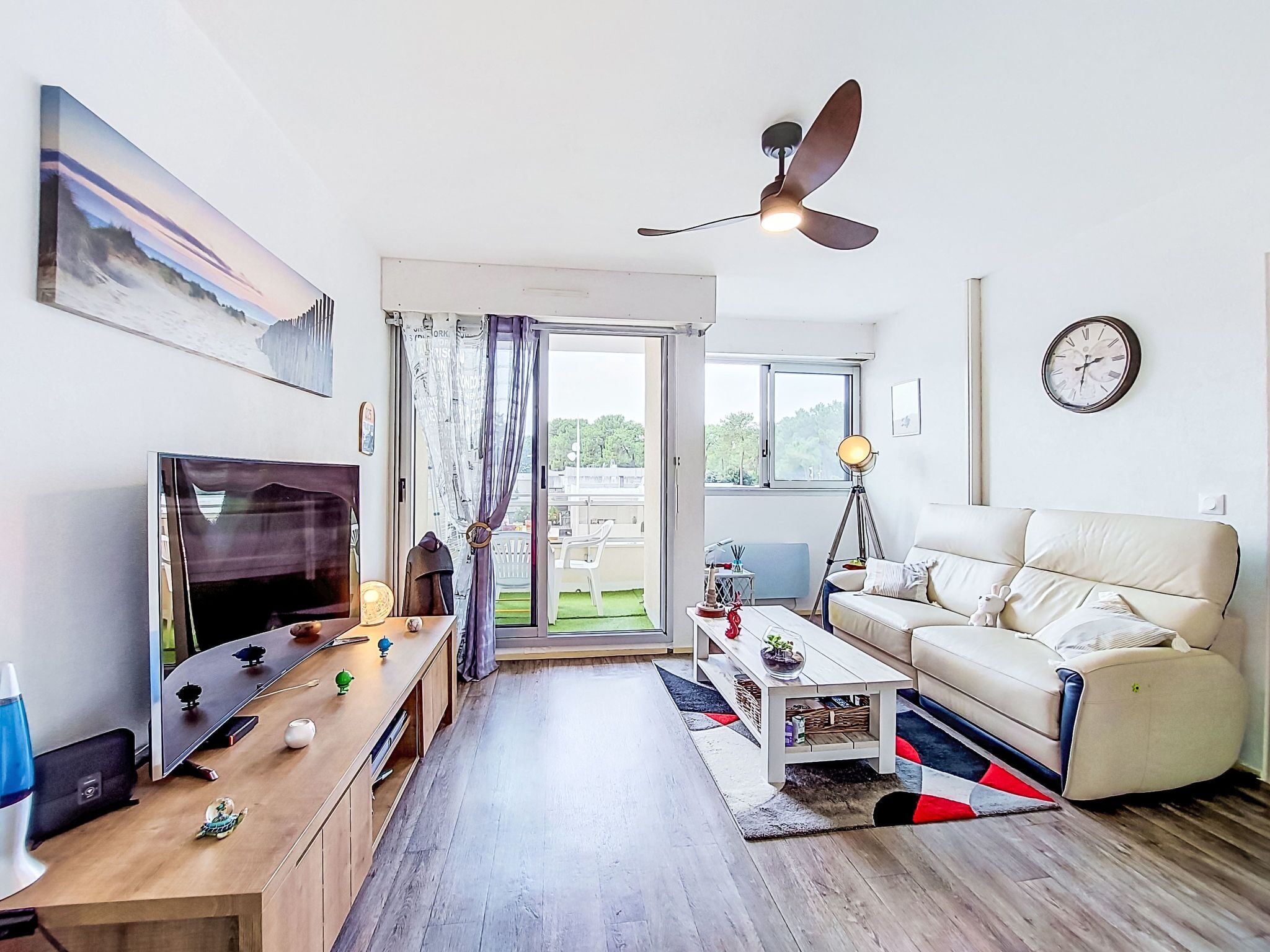 A modern living room with a flat-screen TV, a ceiling fan, a sofa, and a dining table.