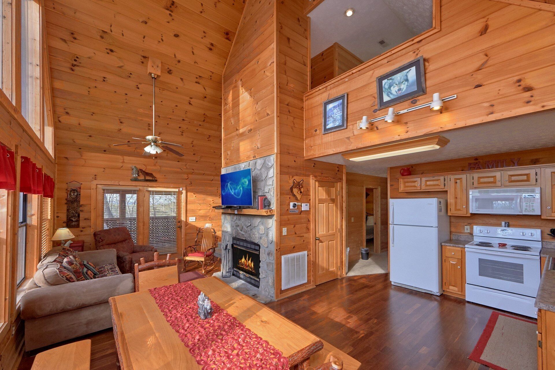 Een chaletinterieur met een open haard, houten wanden, een eethoek en een keuken met apparatuur.
