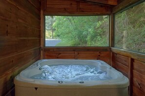 A wooden cabin with a hot tub and a window overlooking a forested area. - Absolute Heaven Cabin Rental (Wears Valley)