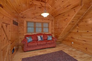 A log cabin interior with a red sofa, a window with blinds, and a hanging light fixture. - Absolutely Viewtiful Cabin Rental (Sevierville)