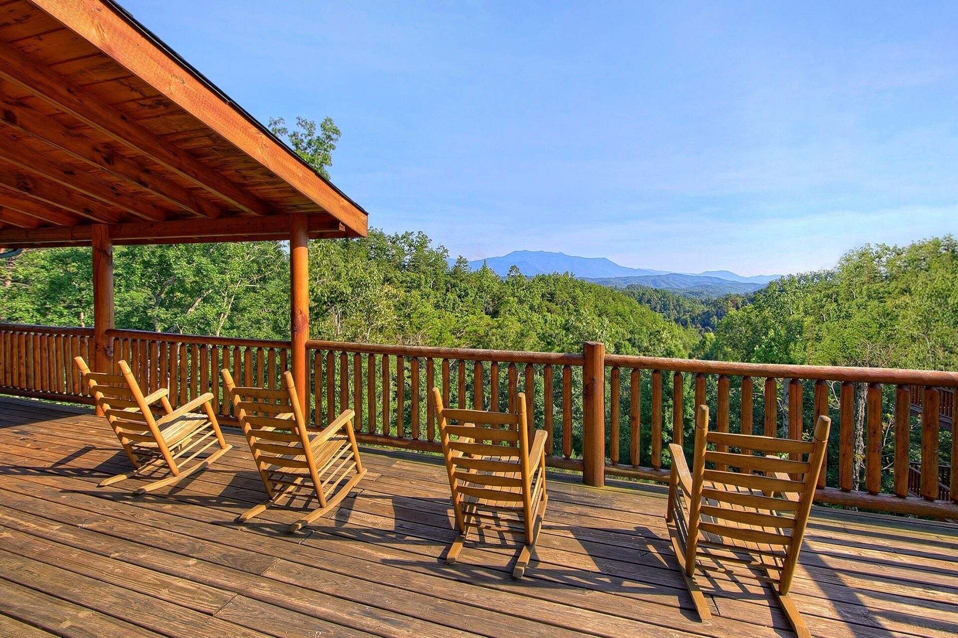 Terraza de madera con cuatro mecedoras y vista a una cadena montañosa boscosa.