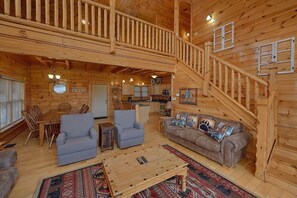 A wooden cabin interior with a dining area, two sofas, a coffee table, and a staircase. - Absolutely Viewtiful Cabin Rental (Sevierville)