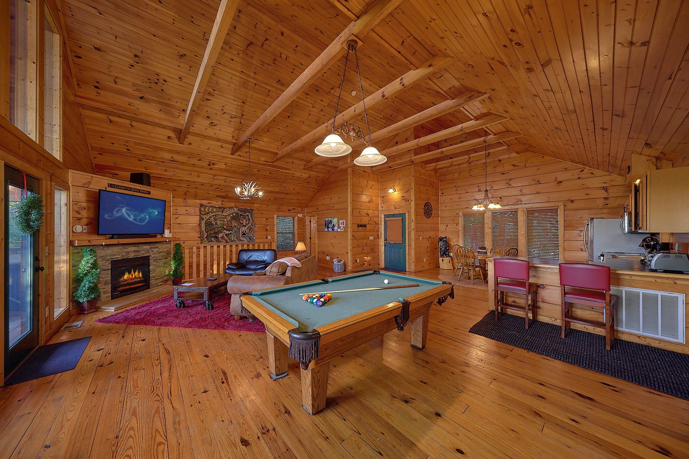 A wooden cabin interior with a pool table, seating area, fireplace, and a television.
