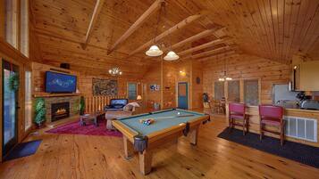 A wooden cabin interior with a pool table, seating area, fireplace, and a television.