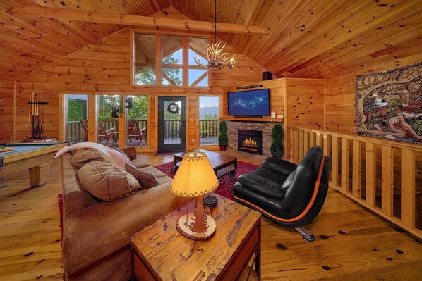 A cozy wooden cabin interior with a fireplace, a television, a pool table, and a comfortable seating area.