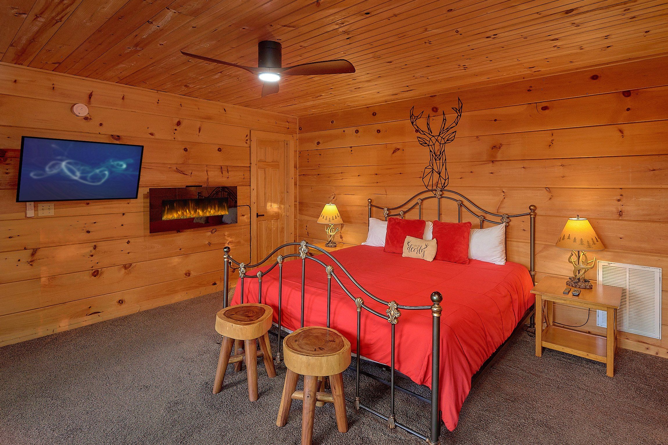 Un dormitorio de cabaña de madera con una cama, dos taburetes, un televisor y una chimenea.