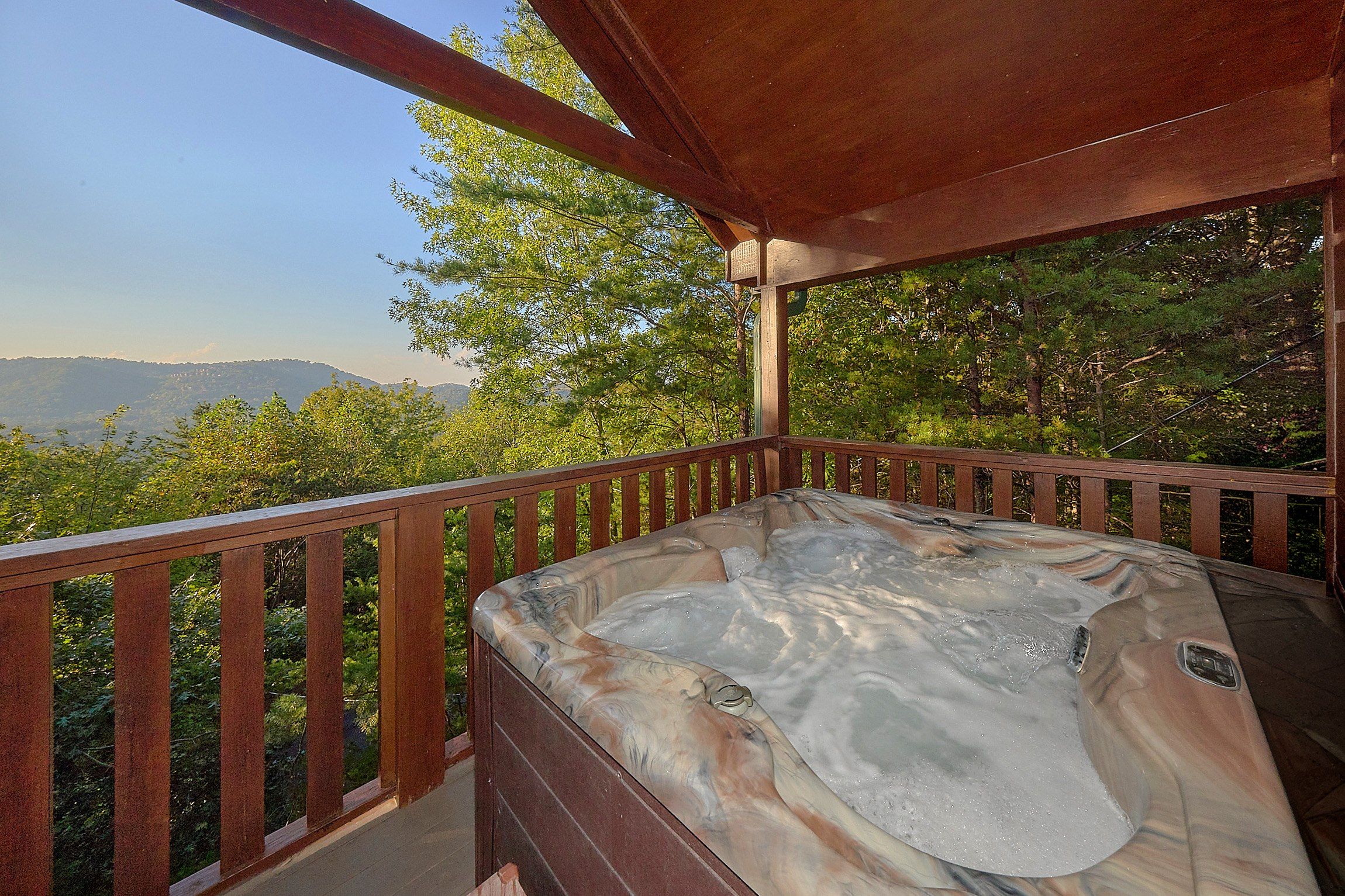 A hot tub on a wooden deck with a view of mountains and trees.