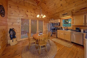 A wooden cabin interior with a dining area, kitchen, and a large window.