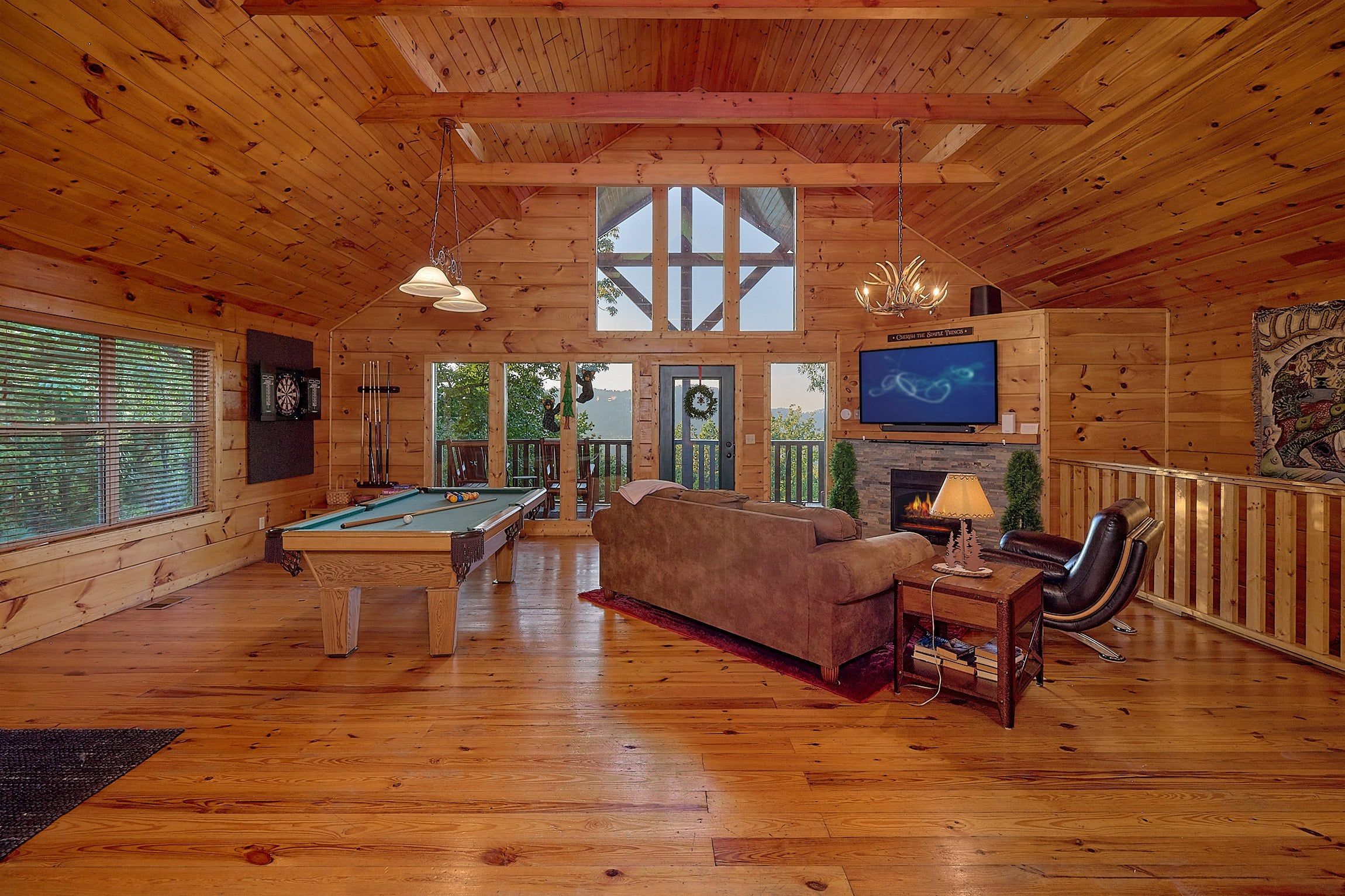 A wooden interior with a pool table, sofa, television, and a fireplace.