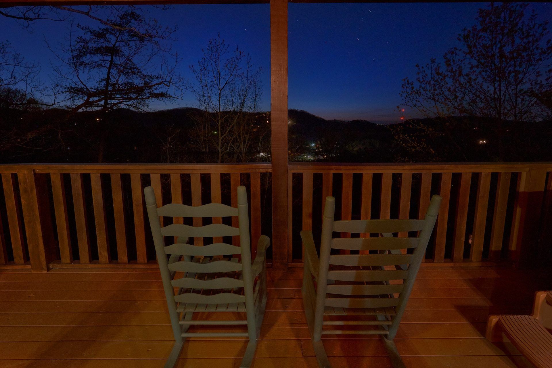 Deux fauteuils à bascule sur une terrasse en bois, avec vue sur une colline et une lumière lointaine.