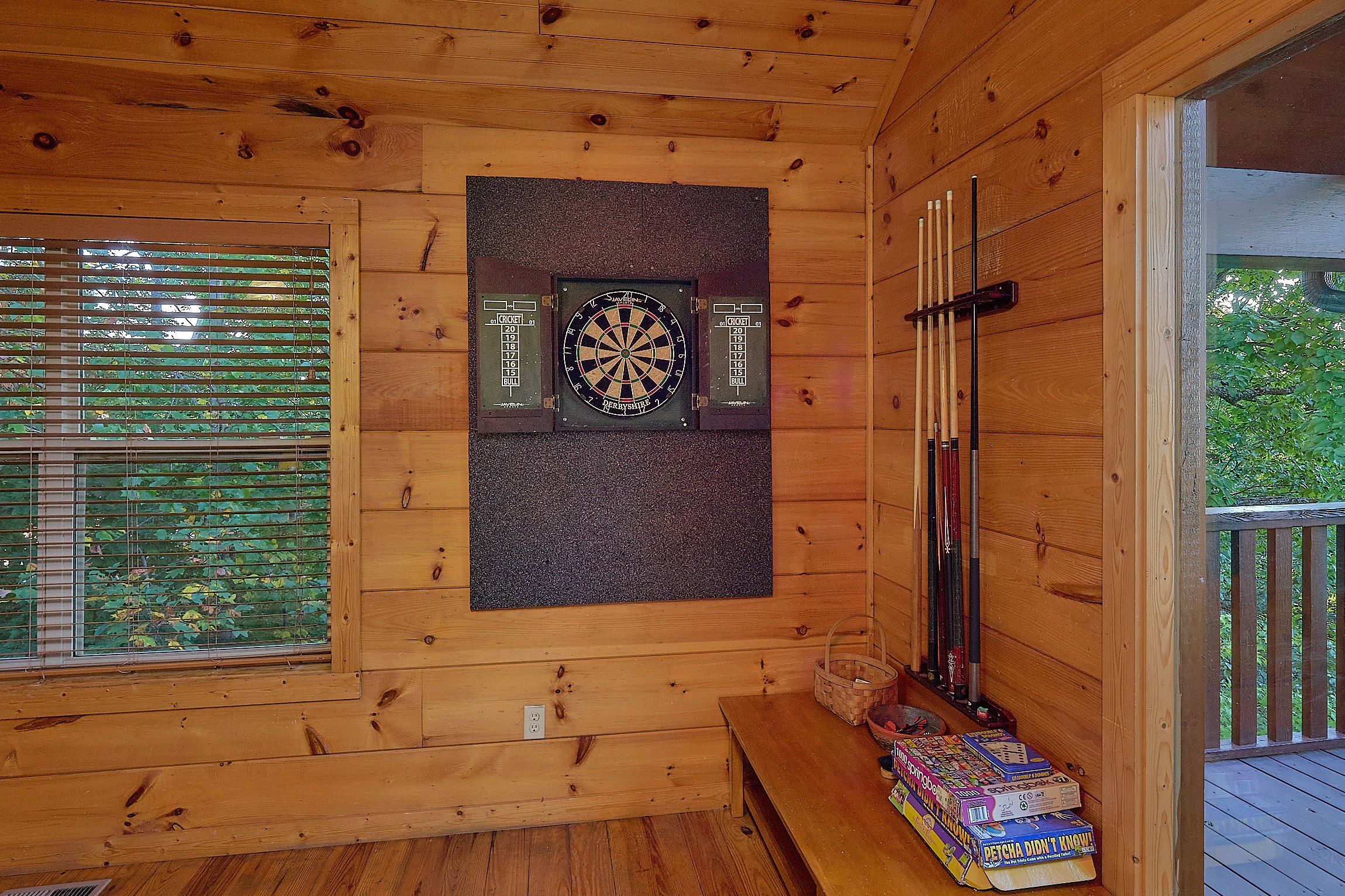 Una habitación de madera con dardos, una ventana con persianas y una mesa con juegos de mesa.