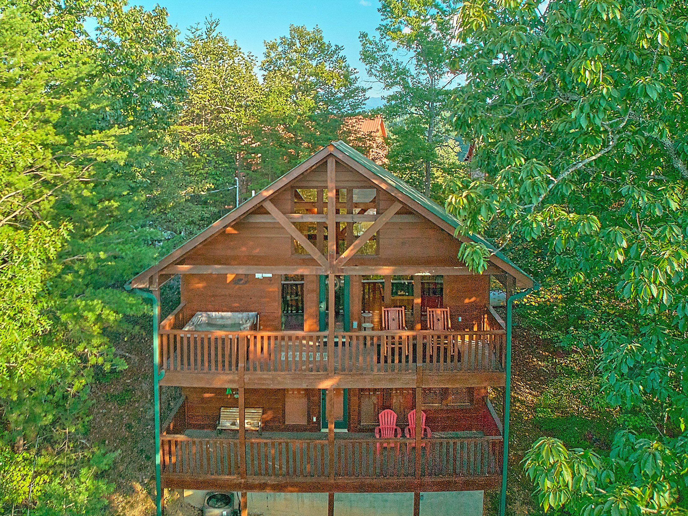 A two-story wooden cabin with a balcony on the upper floor, surrounded by dense foliage.