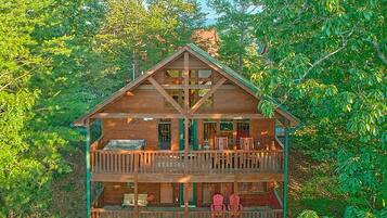 A two-story wooden cabin with a balcony on the upper floor, surrounded by dense foliage.