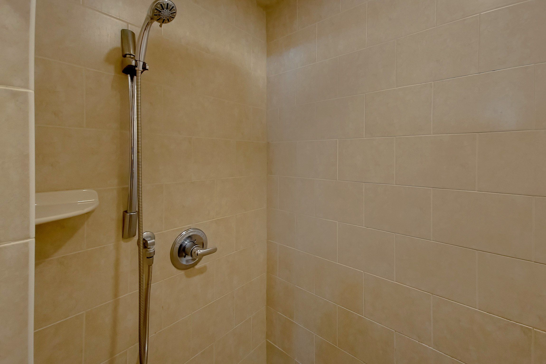 A shower with a handheld showerhead and a wall-mounted control valve.