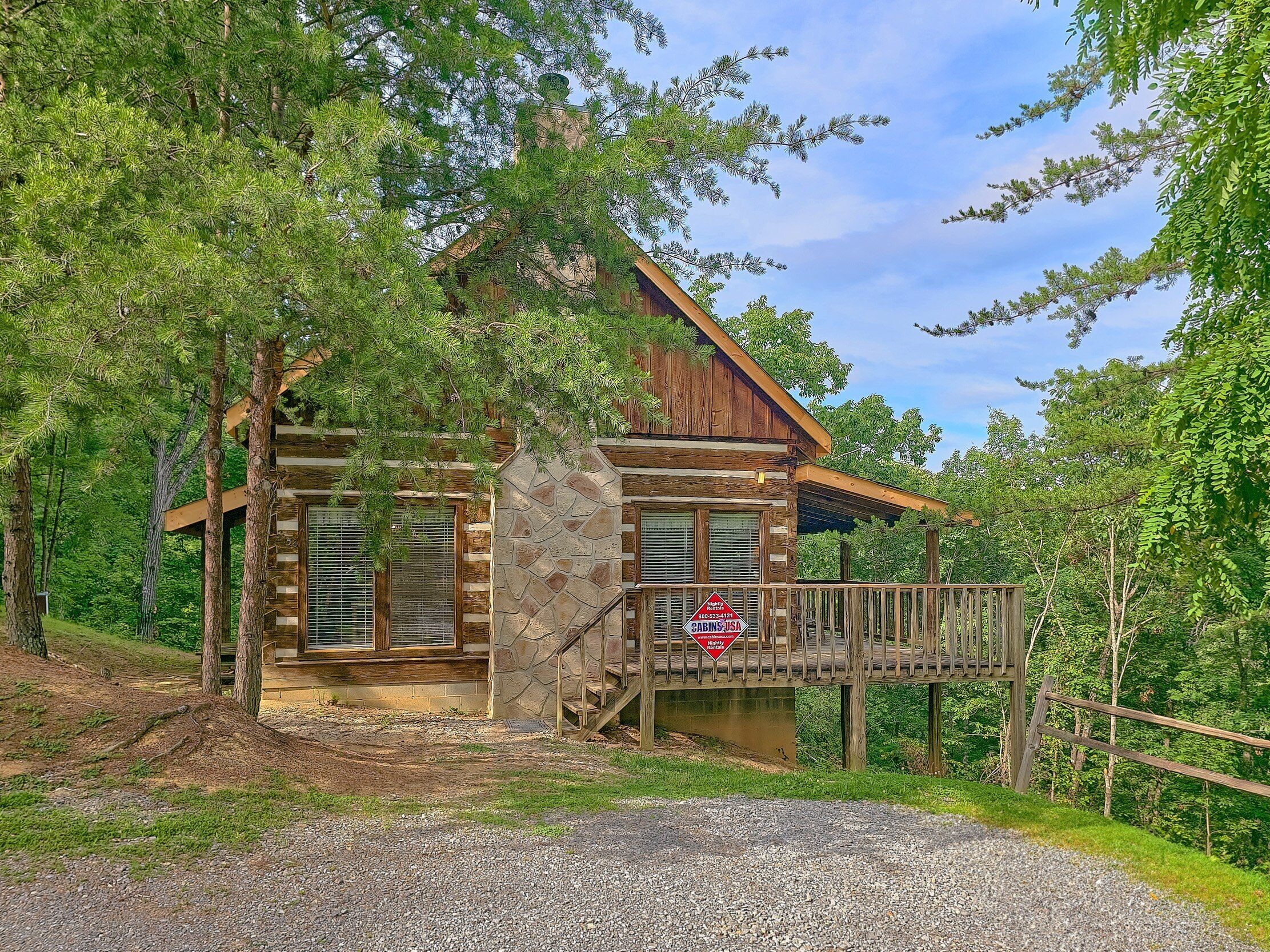 Une cabane en rondins avec des fondations en pierre, une terrasse en bois et un porche couvert.