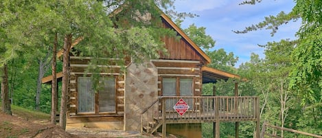 Une cabane en rondins avec des fondations en pierre, une terrasse en bois et un porche couvert.