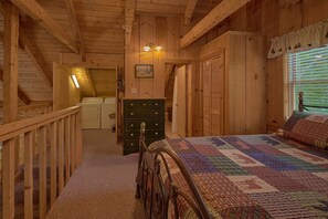 A wooden cabin bedroom with a bed, dresser, and a staircase leading to an upper level. - All By Grace Cabin Rental (Wears Valley)