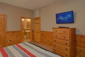 A bedroom with wooden furniture, a television, and a striped bedspread. - Almost Heaven Cabin Rental (Pigeon Forge)
