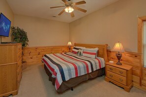 A bedroom with a wooden bed, two bedside tables with lamps, a ceiling fan, a dresser, and a television. - Almost Heaven Cabin Rental (Pigeon Forge)