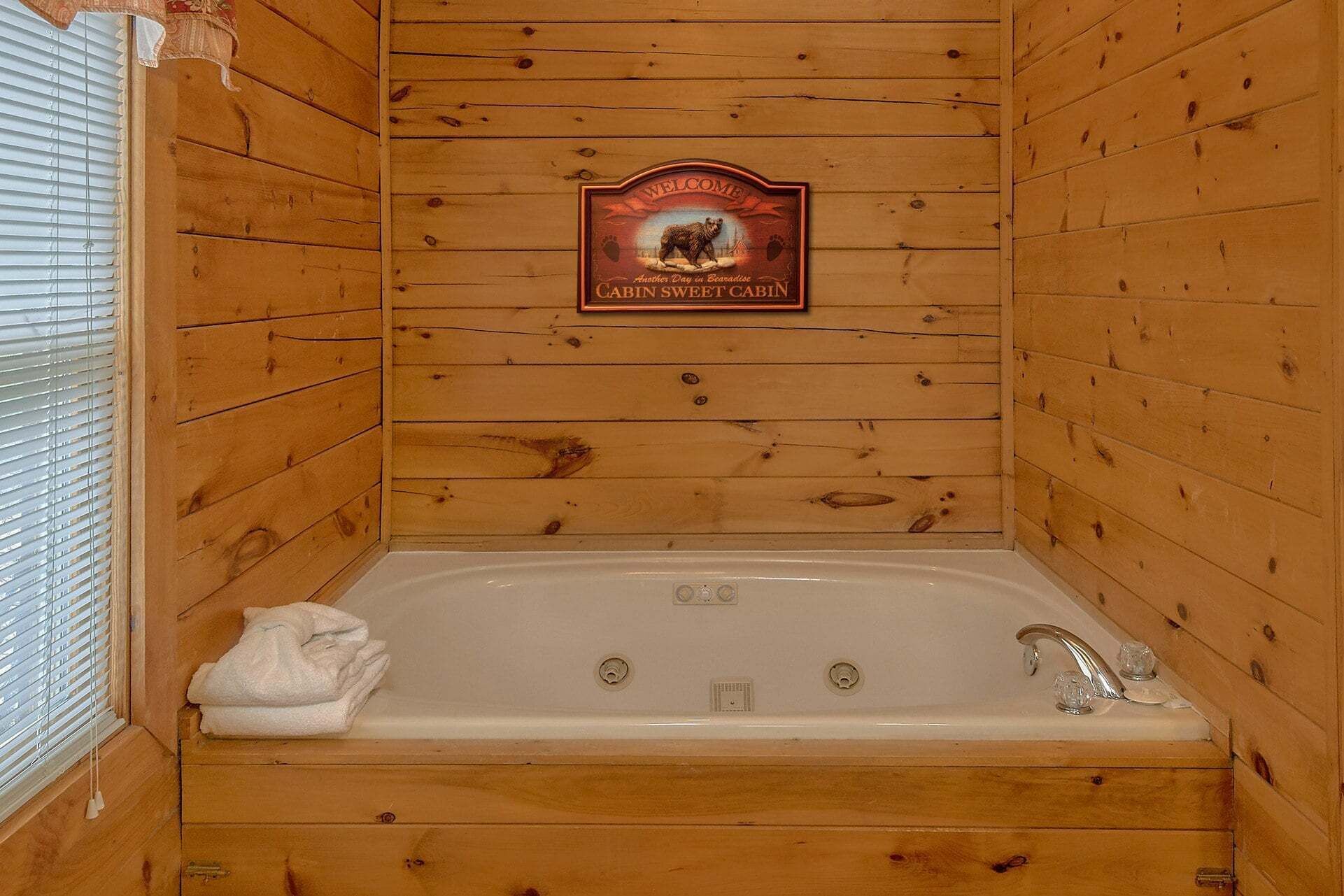 A cabin with a wooden interior, a sign reading 'Welcome Cabin Sweet Cabin,' and a bathtub with a towel on it.